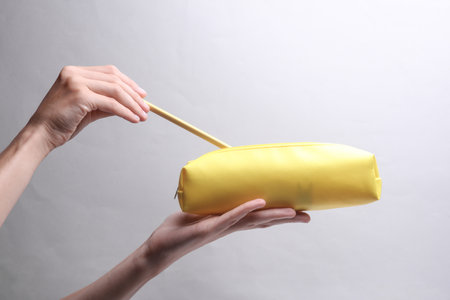 Hand holding yellow pencil case on gray backgroundの写真素材