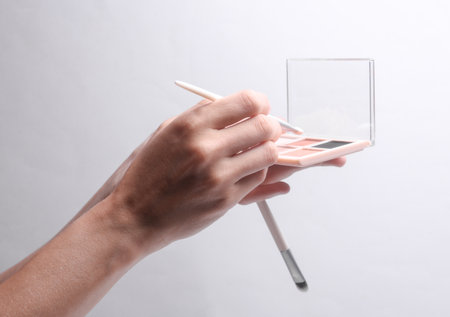Female hands holding makeup palette with brush on gray backgroundの写真素材