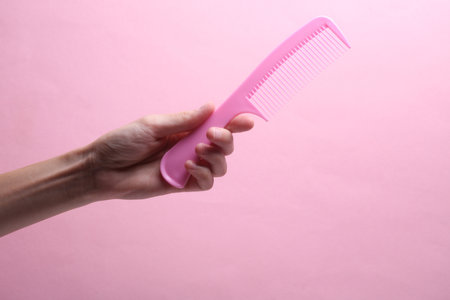 Female hand holding plastic comb on pink backgroundの写真素材