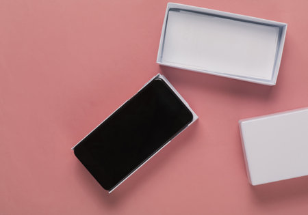 The concept of buying new gadgets. New modern smartphone in a box and mini shopping trolley on pink backgroundの写真素材