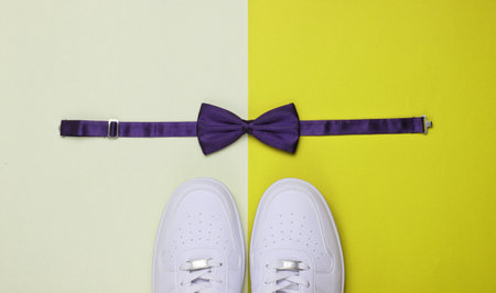 Stylish white sneaker and bow-tie on two-color paper background. Minimalistic fashion concept. Top...