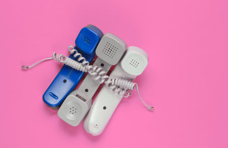 Three office phone tubes wrapped in cable on pink studio background. Call center, hotline conceptの写真素材