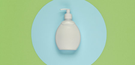 Bottle of liquid soap on colored paper background with geometric shapes. Shower gel, shampoo. Pop...