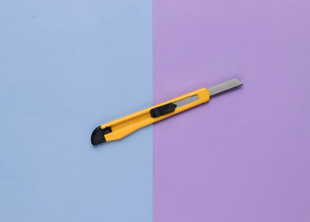 Stationery knife for cutting paper on colored background. Top view