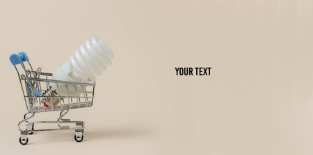 Shopping, eco concept. Shopping trolley with spiral light bulb on beige background. Copy space