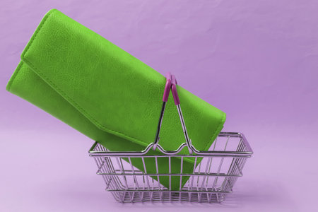 Minimalistic shopping concept. Mini shopping basket and green leather wallet on pink background.