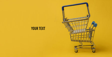 Minimalistic shopping concept. Shopping trolley, basket on yellow background. Copy space