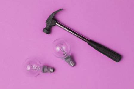 Hammer and old light bulbs on pink background. Top view
