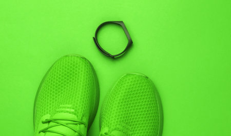 Green sports running shoes and smart bracelet on green paper background. Top view.