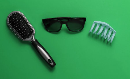 Women's accessories. Sunglasses, comb, hair clip on green background.