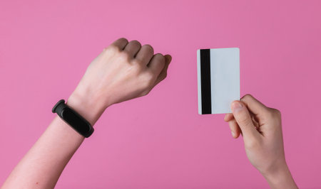 Hand with smart bracelet holding bank card on pink background. Cashless payment, online shopping....