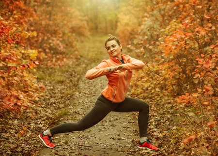 Young attractive sport woman in sportswear doing stretching exercise in autumn forest with reddened...