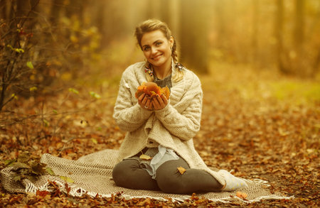 Art portrait. Young attractive woman sits on a plaid and holds fallen leaves in her hands in the...