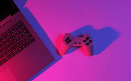Gaming concept. Gaming equipment. Laptop with gamepad. Neon red-blue gradient light. Top view