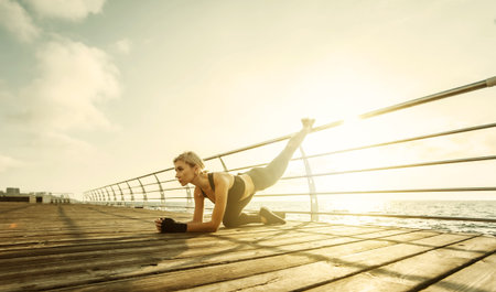 Healthy woman training on seaside promenade. Young attractive woman in sportswear does leg...