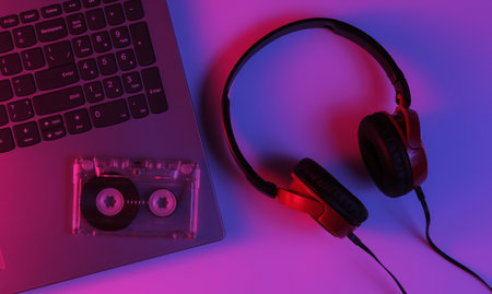Lptop with headphones and audio cassette. Neon blue-red gradient light. Retro wave, pop culture, DJ...