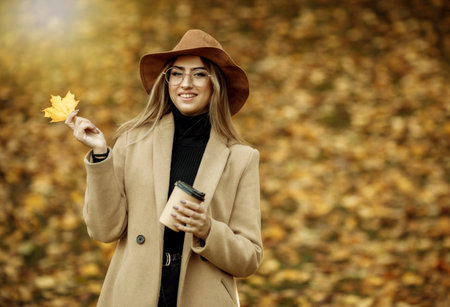 Image-shot of a young attractive woman wearing a coat and felt hat on blurry background of fallen...