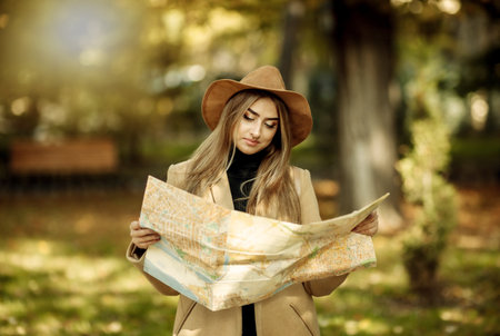 Autumn tourism. Young attractive female traveler is guided by the city map. Beautiful girl looking...