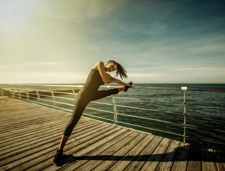 Slim fit woman in sportswear doing stretching legs on the beach at bright sunny dayの写真素材