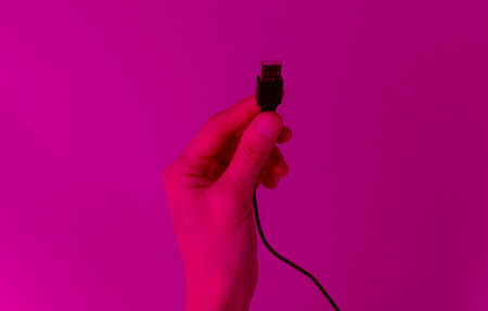 female hand holds usb cable in pink neon light