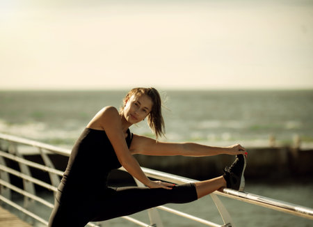 Slim fit woman in sportswear doing stretching legs on the beach at bright sunny dayの写真素材