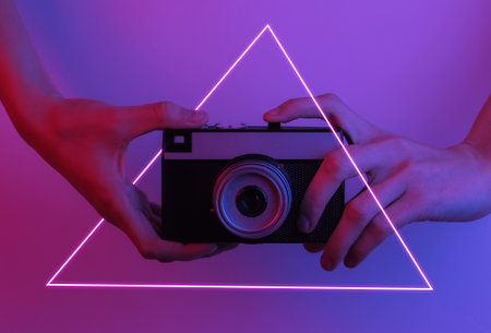 Female hands hold a retro camera. Creative pop art pink blue neon color. Trendy gradient...