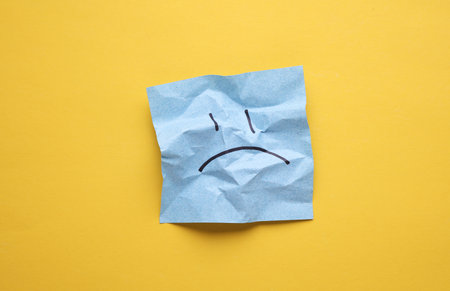 Unhappy face on crumpled square memo paper, yellow background. Business conceptの写真素材