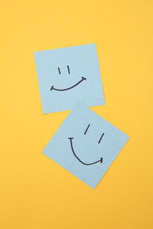 Happy faces on square memo papers, yellow background. Business concept