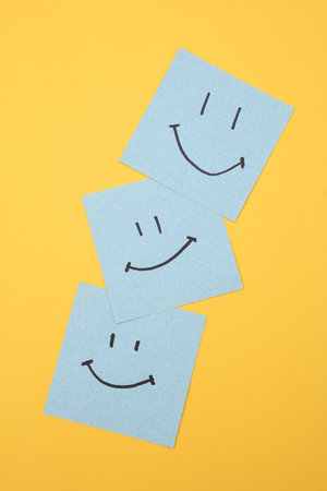 Happy faces on square memo papers, yellow background. Business concept