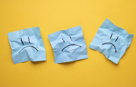 Unhappy faces on crumpled square memo papers, yellow background. Business concept