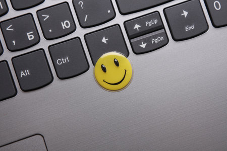 ODESSA, UKRAINE - AUGUST 25, 2023: Round yellow emoticon smiling sticker and laptop