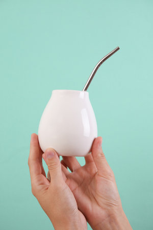 Female hand holding bombilla with white calabash for mate on blue background. Mockup for design
