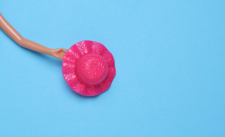 Doll hand holding hat on blue background