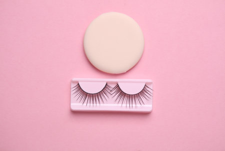 False eyelashes and makeup sponge on pink background. Beauty concept