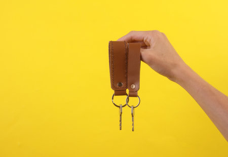 Leather keychains with keys in female hand on yellow background