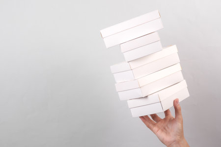 Female hand holding stack of white cardboard boxes on gray background. Food delivery, branding, mockupの写真素材