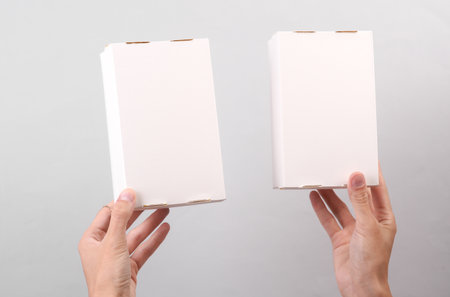 Female hands holding white cardboard boxes on gray background. Food delivery, branding, mockup