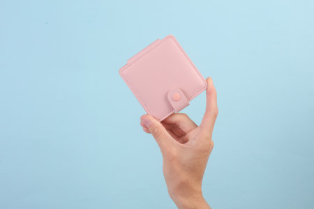 Female hand holding pink leather wallet on blue background