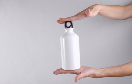 White metal water flask, thermos bottle in hand on gray background. Mockup for designの写真素材