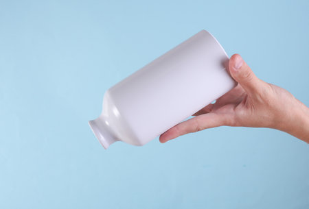 White metal water flask, thermos bottle in hand on blue background. Mockup for designの写真素材