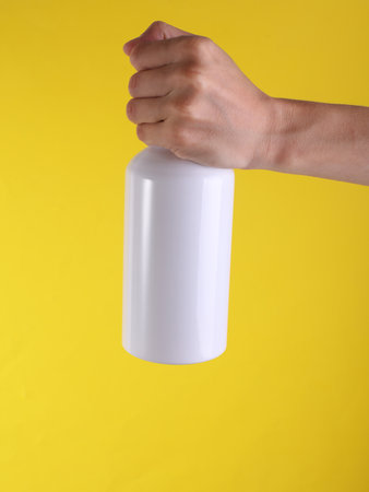 White metal water flask, thermos bottle in hand on yellow background. Mockup for designの写真素材