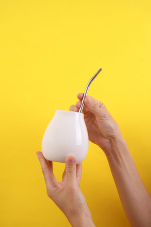 Female hand holding bombilla with white calabash for mate on yellow background. Mockup for design