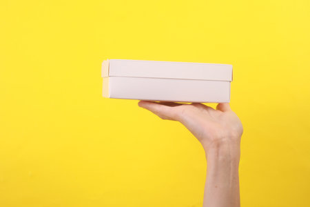 Female hand holding white cardboard box on yellow background
