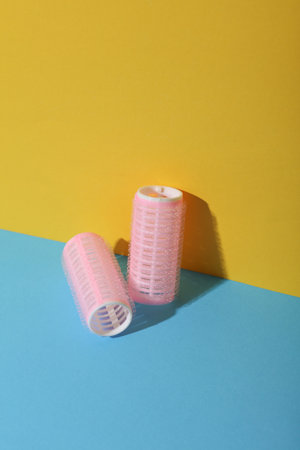 Plastic hair curlers on yellow and blue background. Beauty concept, creative layoutの写真素材