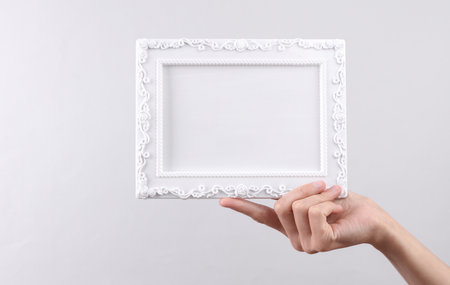 Hand holding white blank Ornamental photo frame on gray background