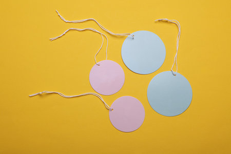 Round blue and pink price tags on ropes, yellow background