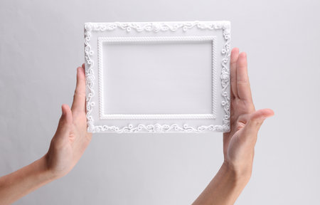 Hands holding white blank Ornamental photo frame on gray background