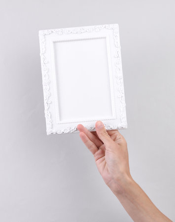 Hand holding white blank Ornamental photo frame on gray background