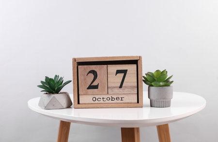 Wooden calendar organizer with date October 27 and decorative plants on table
