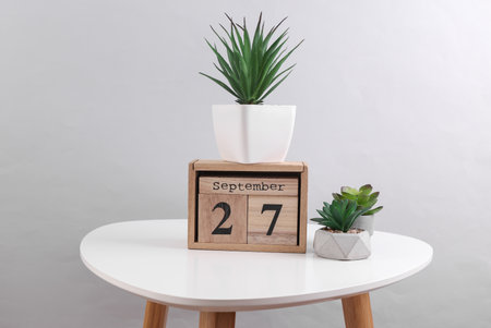 Wooden calendar organizer with date September 27 and decorative plants on table